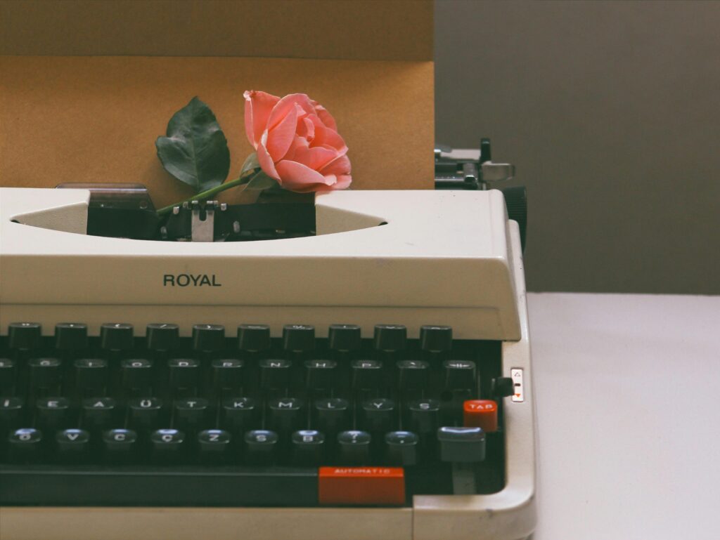 A vintage typewriter holds a pink rose and a letter, evoking nostalgia and romance.