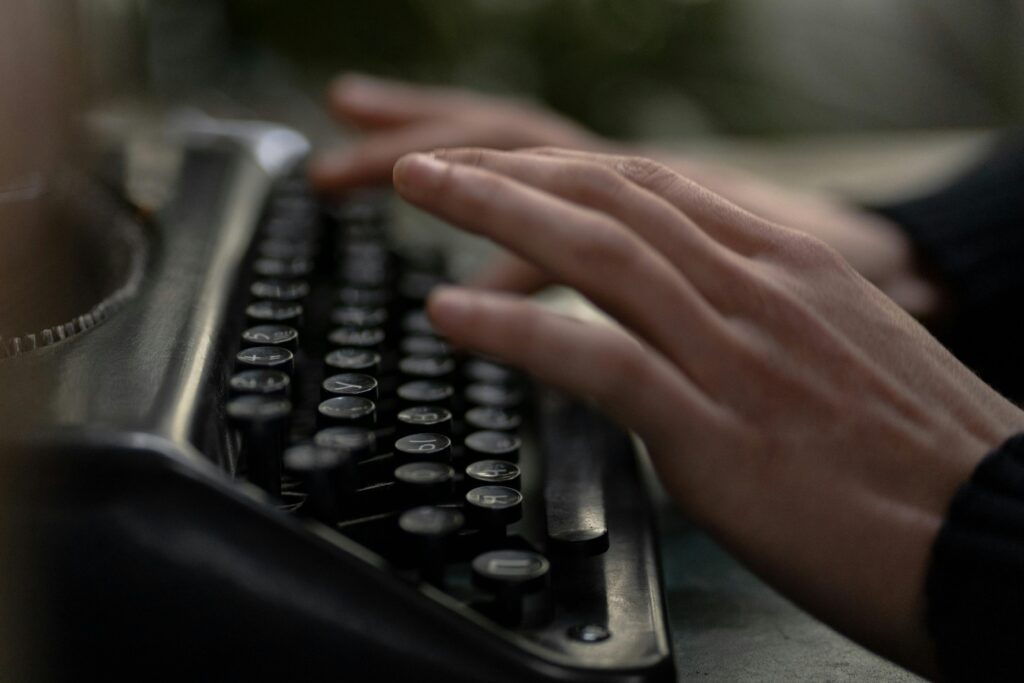 Close-up of hands typing on an old-fashioned typewriter, evoking nostalgia and creativity.