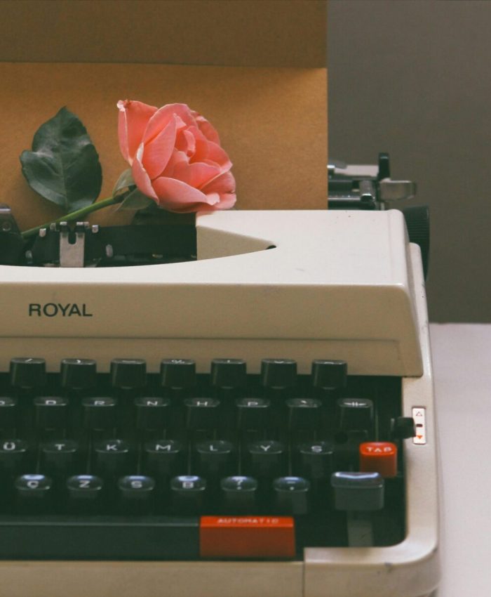A vintage typewriter holds a pink rose and a letter, evoking nostalgia and romance.