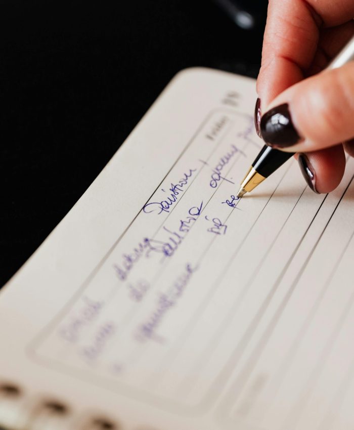 Closeup of crop anonymous lady with black manicure writing in planner with elegant pen